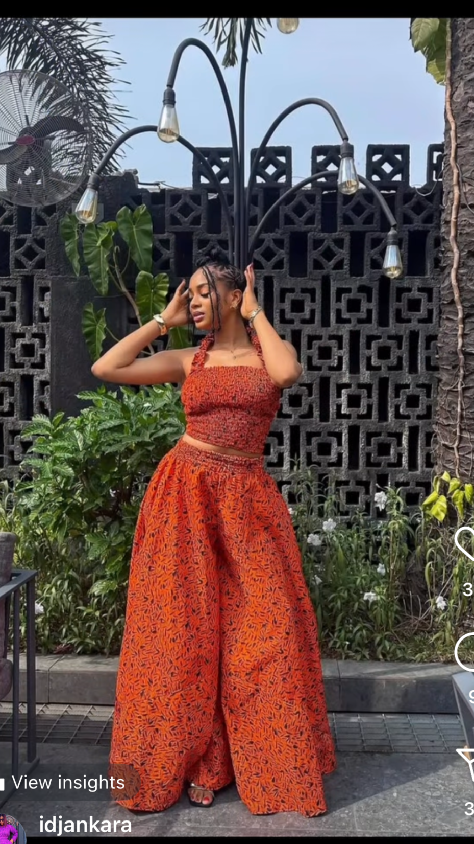 Woman in an orange dress standing outdoors with a decorative wall and plants in the background