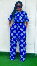 Woman wearing a blue and white floral jumpsuit standing against a white wall.