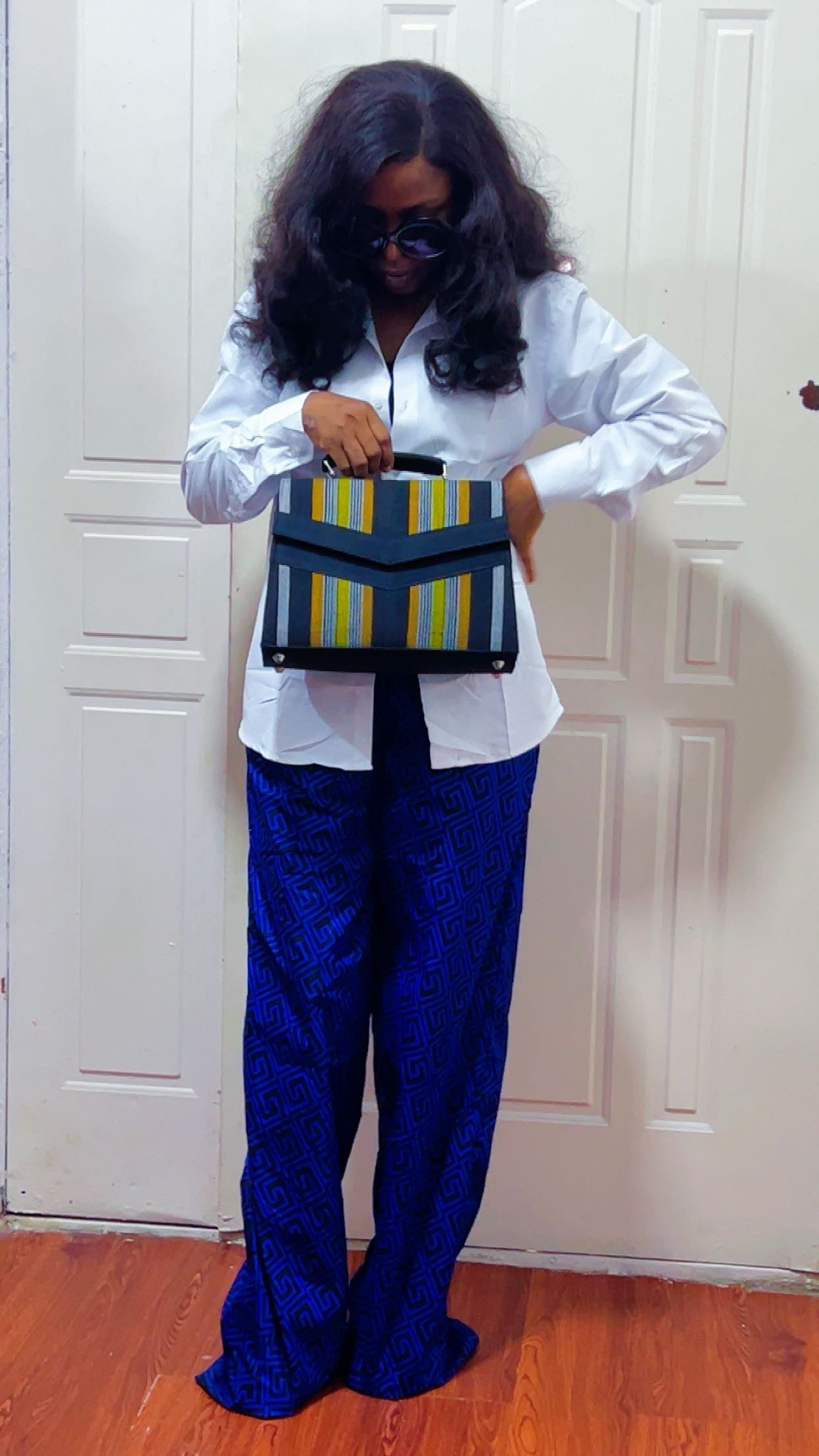 Person wearing a white shirt and blue pants holding a black and yellow bag against a white door background.