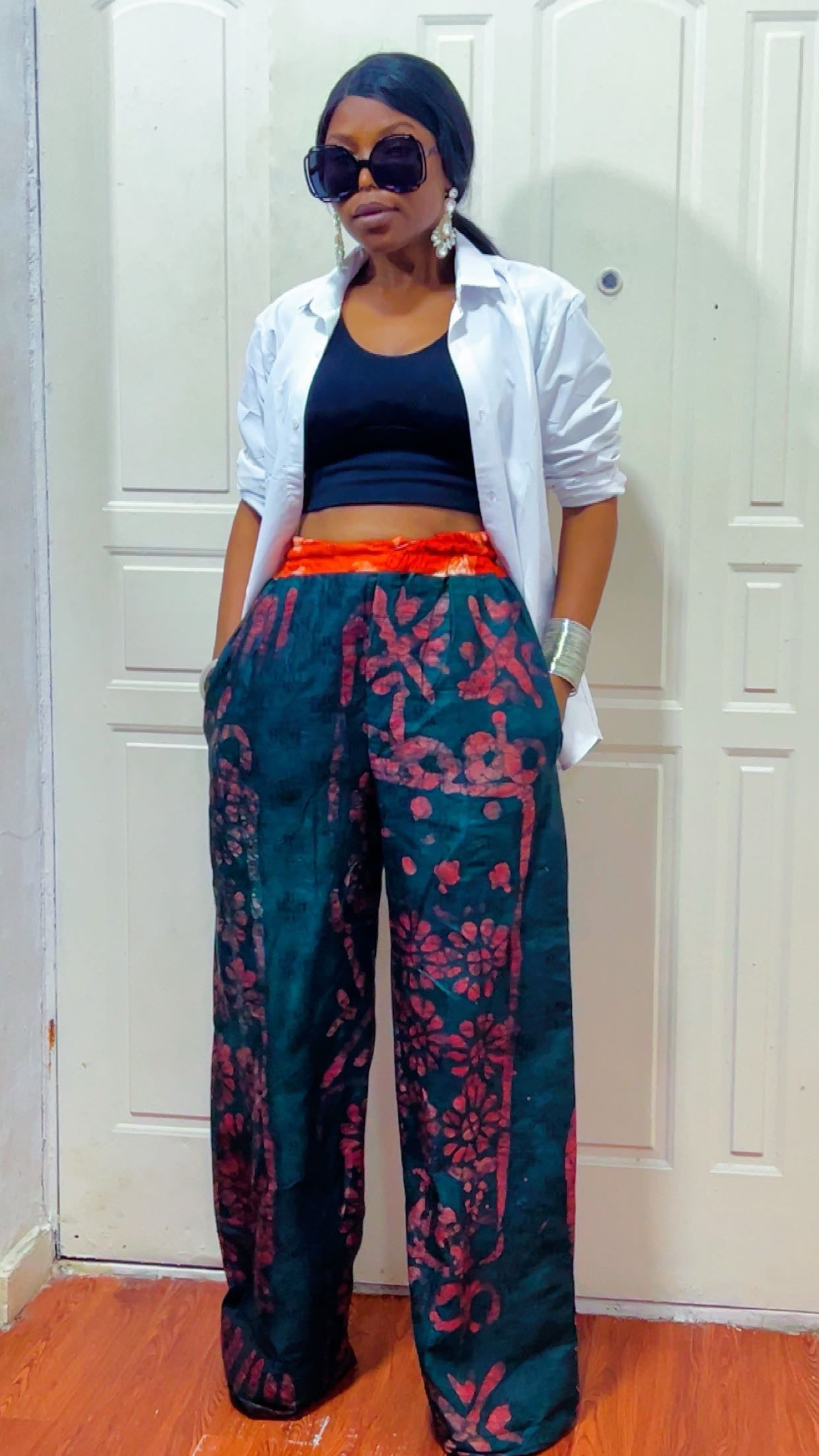 Woman wearing a white shirt, black top, and colorful pants in front of a white door.