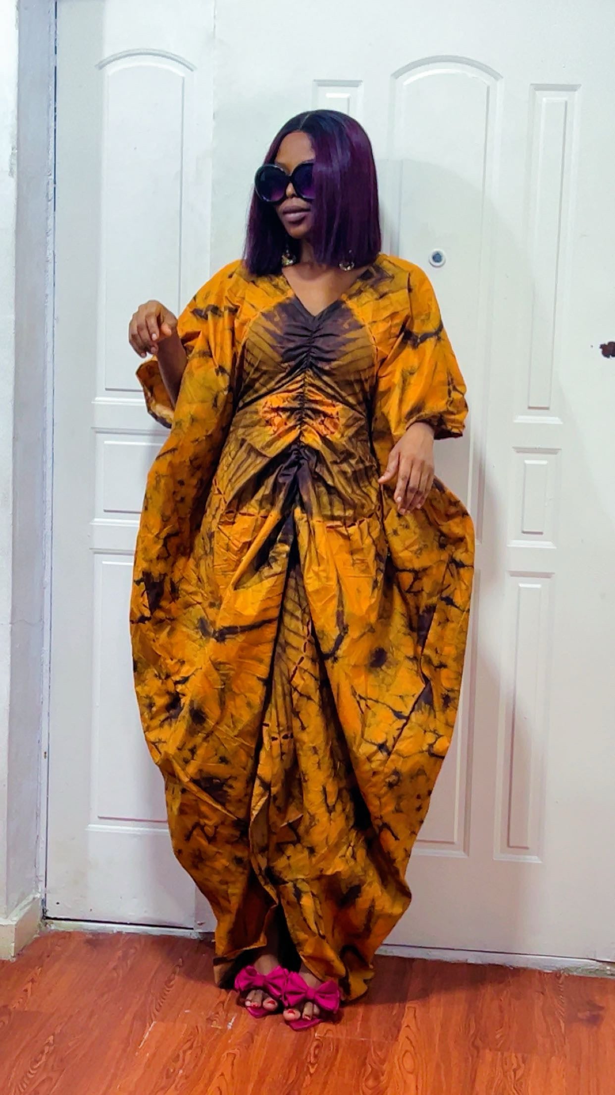 Woman wearing a mustard yellow and black patterned dress standing in front of a white door.