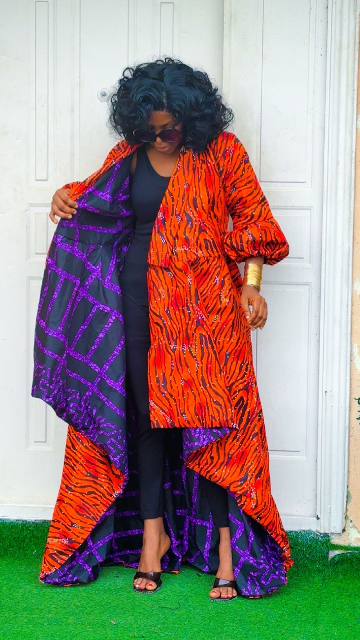 Woman wearing a colorful patterned coat with an orange and purple design, standing against a white wall.